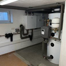 Ein moderner Heizungsraum mit einer weißen Heizungsanlage und mehreren Rohren, die an die Wand montiert sind.
