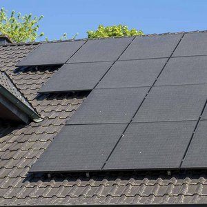 Ein modernes Hausdach mit mehreren Solarpanelen, die in der Sonne glänzen, umgeben von frischem Grün im Hintergrund.