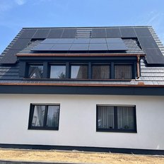 Ein modernes Haus mit einem schrägen Dach, das mit Solarpanelen ausgestattet ist, unter einem klaren blauen Himmel.