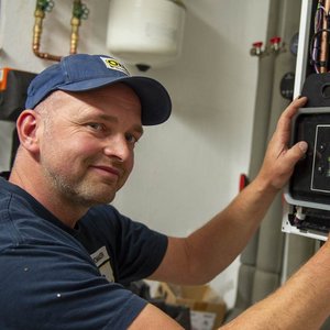 Ein Handwerker lächelt, während er an einem modernen Heizgerät arbeitet und einen Regler anpasst.