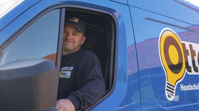 Ein Handwerker lächelt freundlich aus dem Fenster eines blauen Lieferwagens mit dem Logo der Firma Otte.