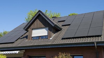 Ein modernes Haus mit einem schrägen Dach, das mit mehreren Solarpanelen bedeckt ist, unter einem strahlend blauen Himmel.