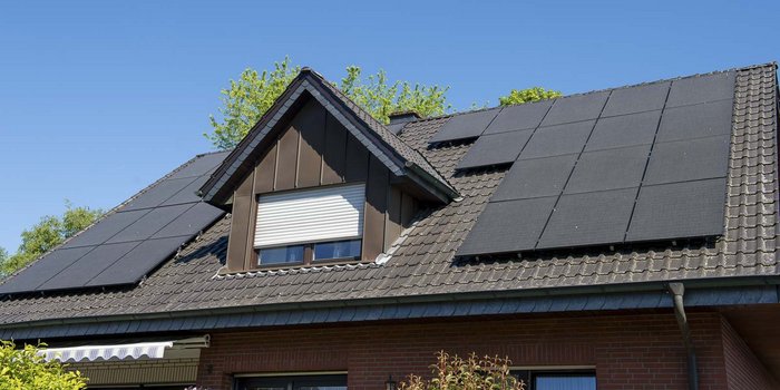 Ein modernes Haus mit einem schrägen Dach, das mit mehreren Solarpanelen bedeckt ist, unter einem strahlend blauen Himmel.