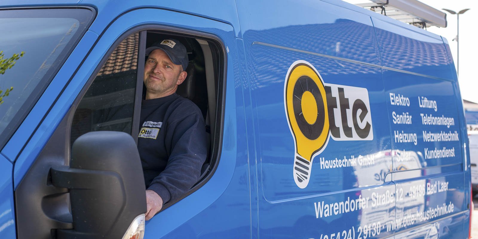 Ein Mann sitzt am Steuer eines blauen Lieferwagens mit dem Logo einer Haustechnikfirma, bereit für den nächsten Auftrag.
