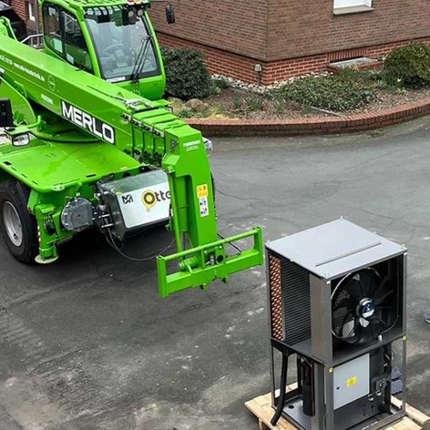 Ein grüner Teleskoplader steht auf der Straße, während ein Mann in einem grauen Mantel daneben steht und beobachtet.