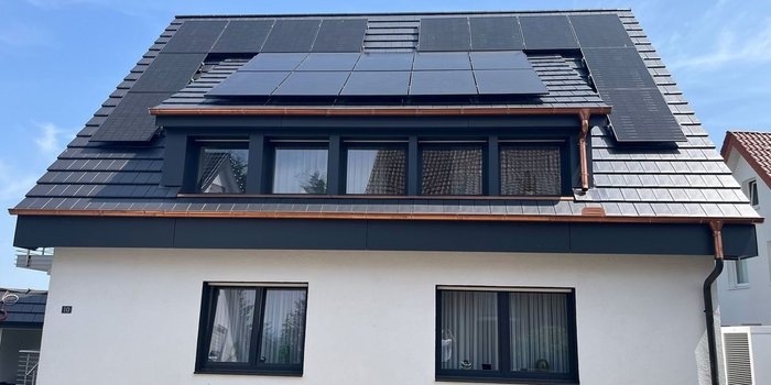 Ein modernes Haus mit einem schrägen Dach, das mit Solarpanelen ausgestattet ist, unter einem klaren blauen Himmel.