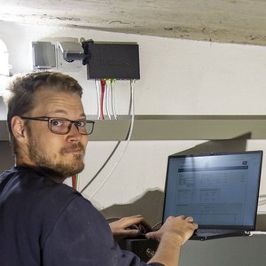 Der Mann mit Brille schaut auf seinen Laptop, während er in einem gut beleuchteten Keller an einem Projekt arbeitet.