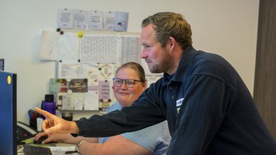 Ein Mann zeigt mit dem Finger auf den Bildschirm, während eine Frau lächelnd daneben sitzt und aufmerksam zuschaut.