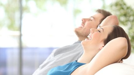 Ein lächelndes Paar entspannt auf einer Couch, genießt den Moment und strahlt Freude und Zufriedenheit aus.