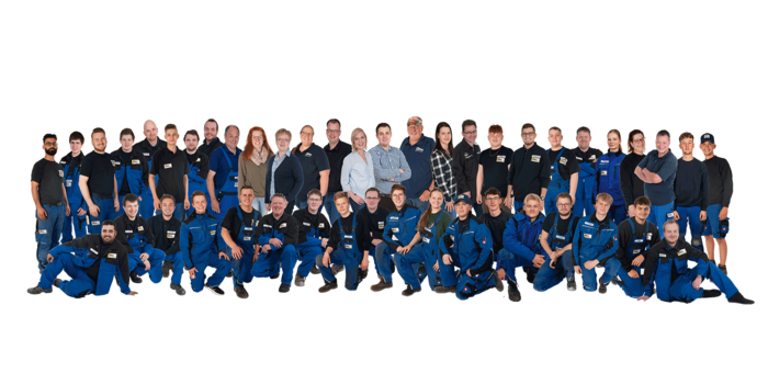 Eine große Gruppe von Menschen in blauen Arbeitsanzügen steht zusammen und lächelt in die Kamera, einige tragen Namensschilder.