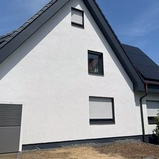 Ein modernes, weißes Haus mit einem schrägen Dach und Solarzellen, unter einem strahlend blauen Himmel.